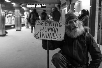 A homeless eprson with a sign that reads 'seeking human kindness'.